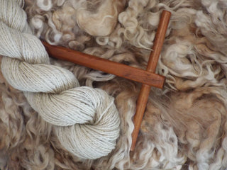 Cream-white wool yarn and un-processed sheep wool with wooden spinning tool.