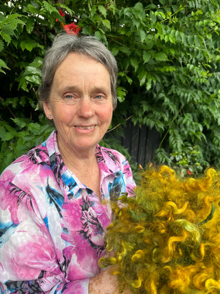 Spinning tutor Anne Grassham smiles holding a bundle of yellow sheep wool.