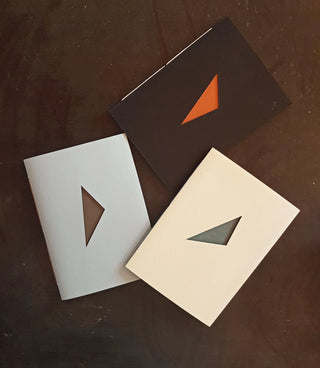 Three books bound in different colours with triangular windows cut out of the front.