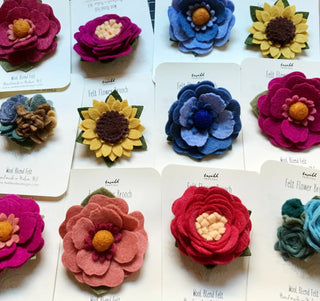 A variety of flower brooches made from felt, pinned onto white cards.