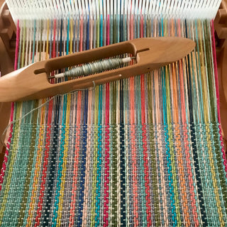 Hand loom halfway through weaving a dishcloth or washcloth in a rainbow of colours.