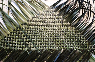 Progress shot of kete whakairo, with light green and dark green flax woven together in tight grid pattern.