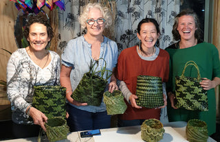 Students smiling, holding up their finished kete whakairo (flax baskets) at the end of the workshop.