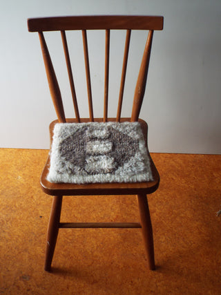 A small natural grey and brown Heirloom Hooked Fleece Rug on the seat of a wooden chair. 
