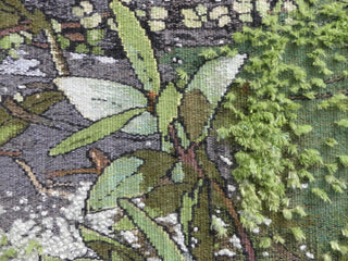 Close-up of a green tapestry depicting native trees, leaves and greenery.