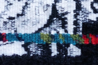 Close up of a white and black tapestry with a thin horizontal bar of green and blue colours.