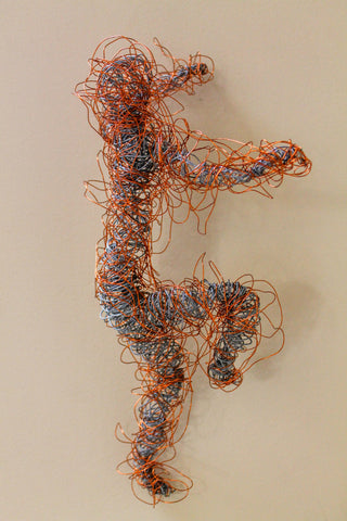An artwork of a running man hung up on a wall, made from interwoven copper-coloured metal.
