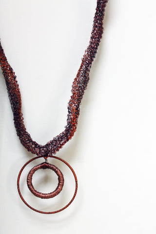 A necklace made from red and black wire with a circular pendant piece.