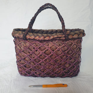 Traditional Māori Kete basket woven with purple brown Harakeke (NZ Flax), next to a pen for scale.