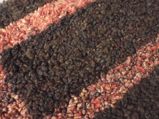 A red and dark brown Heirloom Hooked Fleece Rug with a rectangular pattern, close enough to see the fibres of the wool.